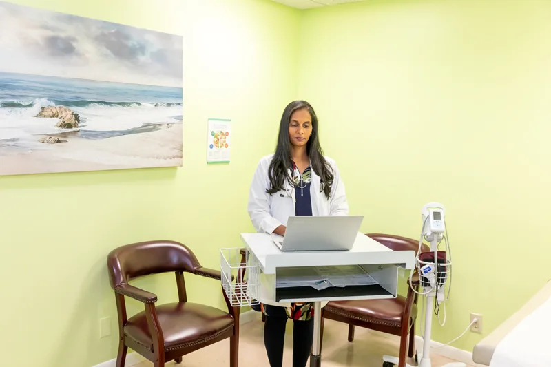 Dr. Siram working at a standing desk with a laptop in a consultation room