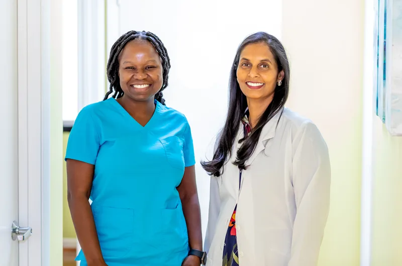 Dr. Gayatri Siram in a white coat standing with a colleague in teal scrubs