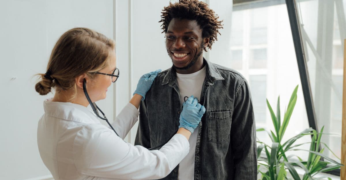 A doctor listening to an adult patient's heartbeat during a consultation