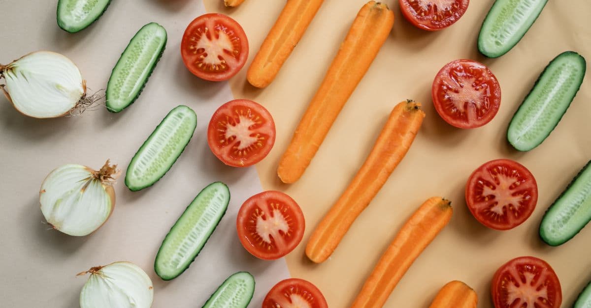 Top view of fresh sliced vegetables including carrots, cucumbers, onions, and tomatoes in a flat lay design.